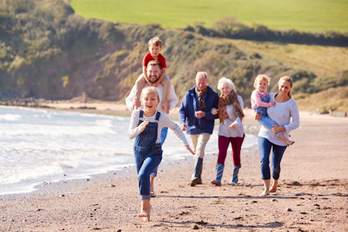 A multi-generation family walk down a beach, smiling and laughing