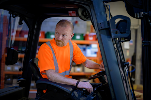 A man operates a forklift, he is wearing a hi-vis t-shirt